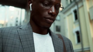 Mutlu bir Afro-Amerikan iş adamının yakın plan görüntüsü. Kablosuz kulaklıkları ile dışarıda yürürken kazanan jestini yaparken cep telefonuna bakıyor.