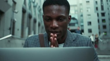 Sokakta ellerini ovuştururken dizüstü bilgisayarıyla çalışan Afro-Amerikalı bir iş adamı.