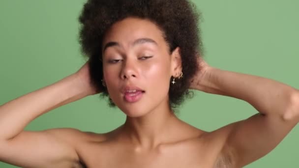 在工作室里 一位漂亮的半裸黑人妇女站在浅绿色的背景上 修整着自己的发型 — 图库视频影像