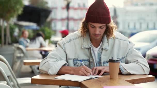 Hombre Concentrado Con Chaqueta Vaquera Escribiendo Cuaderno Sentado Terraza Cafetería — Vídeos de Stock