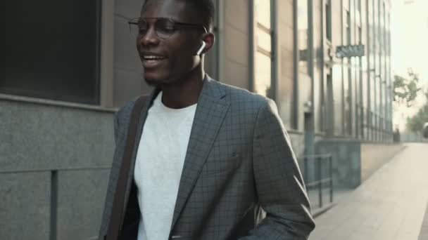 路上でイヤホンを使って音楽を聴いているアフリカ系アメリカ人のビジネスマンが — ストック動画