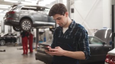 Garajda telefonu kullanan yakışıklı bir tamircinin yan görüntüsü.