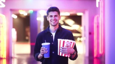 Yakışıklı erkek arkadaş neon salonda elinde patlamış mısır ve kola tutuyor.