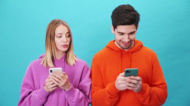 Erkek arkadaşının telefonuna bakan hoşnutsuz bir kadın stüdyoda mavi arka planda dikiliyor.