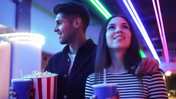 Beautiful couple man and woman walking to the cinema holding a popcorn dating together inside the neon hall — Stock Footage Beautiful Couple Man Woman Walking Cinema Holding Popcorn Dating Together — Stock Video