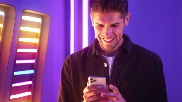 微笑的男人用他的手机站在霓虹灯蓝色的大厅里 — 图库视频影像