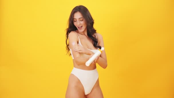 Uśmiechnięta Brunetka Ubrana Strój Kąpielowy Filtrem Przeciwsłonecznym Stojąca Żółtym Tle — Wideo stockowe