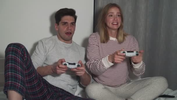二つの幸せな友人男と女遊びコンソールゲーム家に座って — ストック動画
