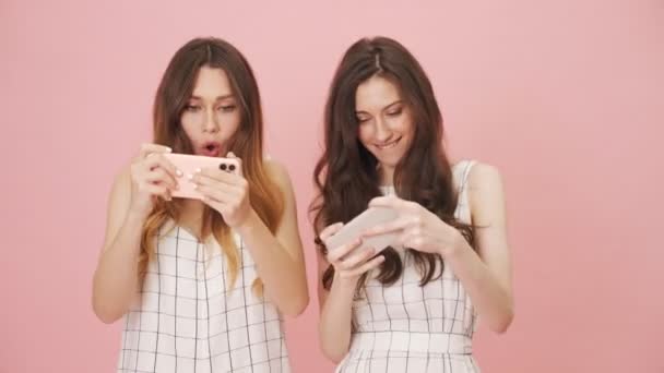 Happy Girls Playing Games Using Mobiles Standing Isolated Pink Background — Stock video