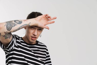 Küpeli genç beyaz adam beyaz arka planda izole edilmiş kameraya bakıyor ve işaret ediyor.