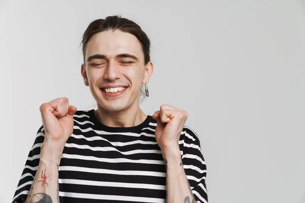 Young white man with earring smiling while making winner gesture isolated over white background