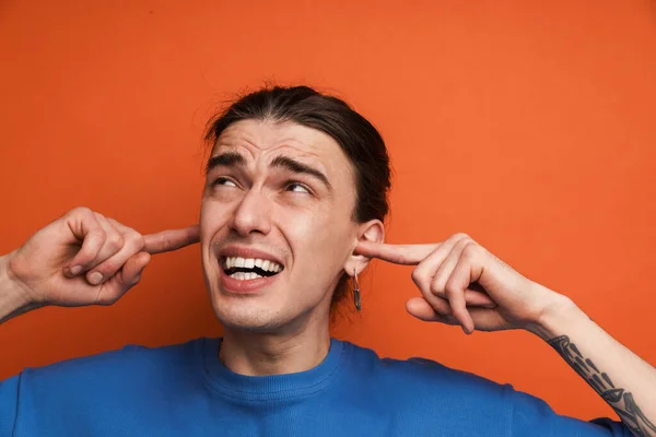 Küpeli Kaşlarını Çatan Kulaklarını Tıkayan Turuncu Arka Planı Olan Genç — Stok fotoğraf