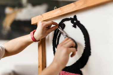 Beyaz adam içeride halı üzerinde çalışırken makas kullanıyor.