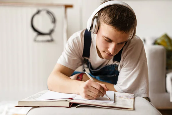 Νεαρός Άντρας Ακουστικά Γράφει Σημειώσεις Ενώ Δούλευε Πάνω Στο Χαλί — Φωτογραφία Αρχείου