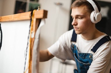 Kulaklıklı genç beyaz adam evde el halısı üzerinde çalışıyor.