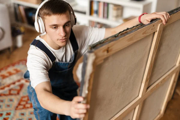Mladý Bílý Muž Sluchátkách Drží Dva Obrazy Doma — Stock fotografie