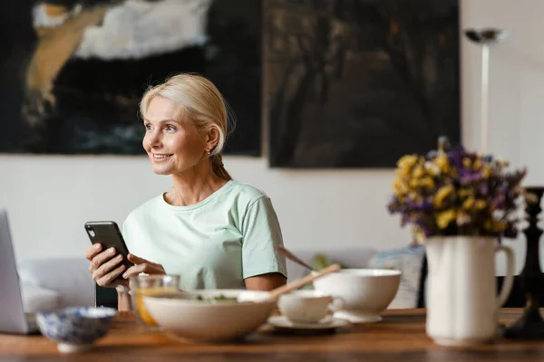 Blond Volwassen Vrouw Met Behulp Van Laptop Mobiele Telefoon Tijdens — Stockfoto