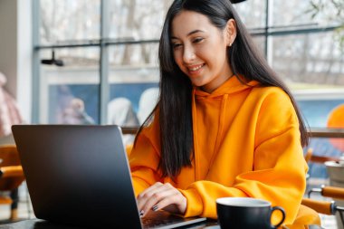 Kafede otururken bilgisayarla çalışan gülümseyen Asyalı kadın.