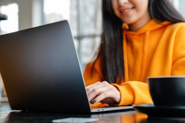 Kafede otururken bilgisayarla çalışan gülümseyen Asyalı kadın.