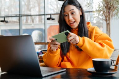 Kafede dizüstü bilgisayarla çalışırken internetten oyun oynayan heyecanlı Asyalı kadın