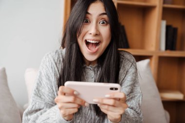 Heyecanlı Asyalı kadın evde cep telefonuyla oyun oynuyor.