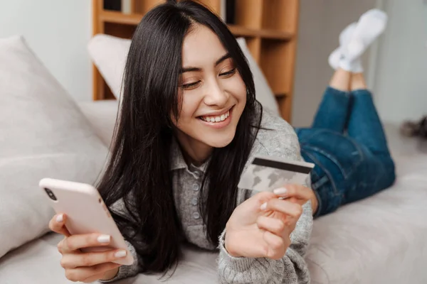 Szczęśliwa Młoda Kobieta Kartą Kredytową Trzyma Telefon Komórkowy Siedząc Kanapie — Zdjęcie stockowe