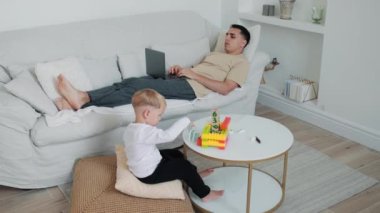 Babası evde çalışırken küçük bir çocuk oyuncaklarıyla oynuyor.