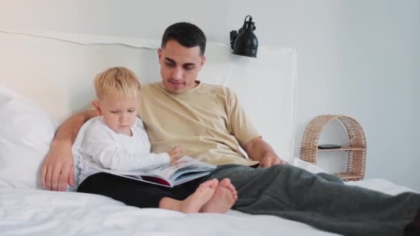 Ένας Πατέρας Διαβάζει Βιβλίο Τον Παιχνιδιάρικο Γιο Του Κάθεται Στο — Αρχείο Βίντεο