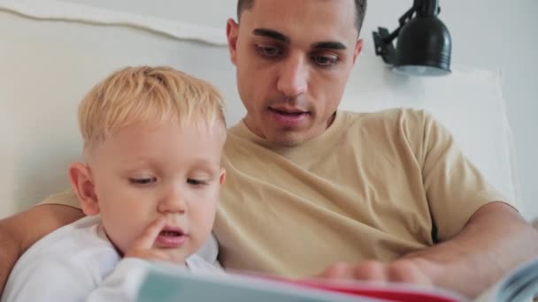 Ein Zufriedener Vater Liest Buch Für Seinen Kleinen Sohn Hause — Stockvideo
