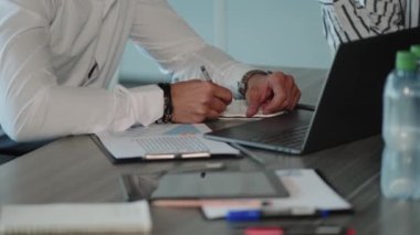 Ofisteki masada oturmuş not alan bir iş adamının kırpılmış görüntüsü.