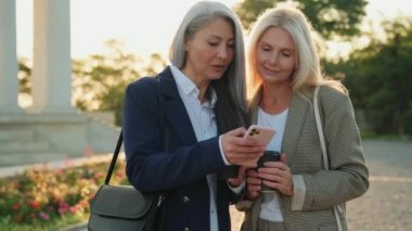 Sokakta yürürken cep telefonu kullanan memnun iş kadınları