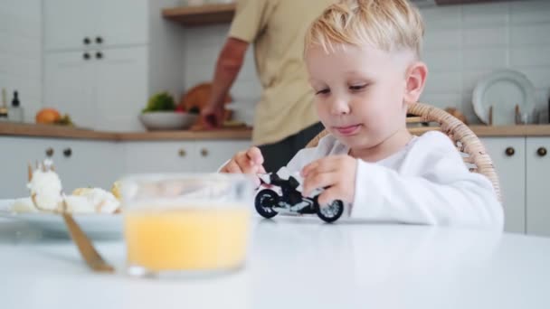 家のテーブルに座って車と遊んでいる男の子 — ストック動画