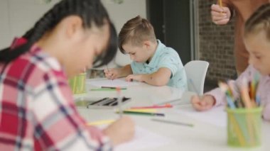Sanat okulundaki masada oturan küçük çocuklar resim çiziyor.