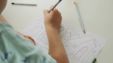 Modern sanat okulunda kalem kullanarak ev çizen küçük bir çocuğun yakın plan görüntüsü.