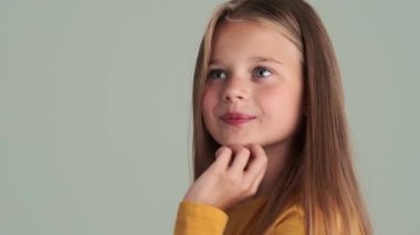 Kameraya bakan utangaç küçük bir kız. Stüdyonun gri duvarından izole edilmiş.