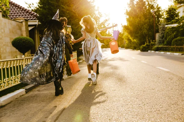 ハロウィンの衣装を着た白い子供たちが屋外でトリックや治療中に通りを歩いています — ストック写真