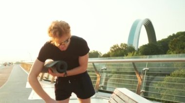 Köprüde yürürken yoga minderi taşıyan bir sporcu.