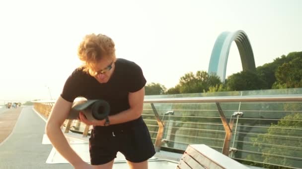 Ein Sportler Trägt Beim Gehen Auf Der Brücke Eine Yogamatte — Stockvideo