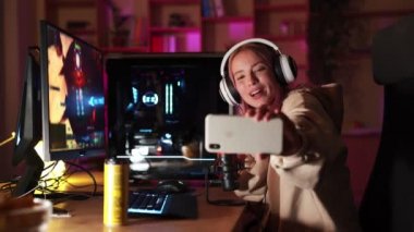 Gülümseyen bir oyuncu kız bilgisayar oyunu oynamadan önce telefonda selfie çekiyor.