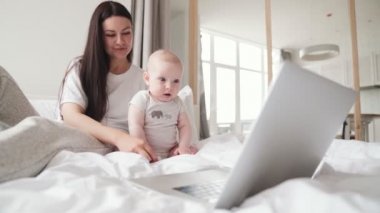 Küçük çocuk annesiyle yatakta otururken dizüstü bilgisayarını değiştiriyor.