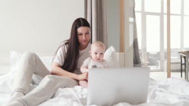 Annesiyle küçük bir çocuk laptopta yatağın üstünde bir şey izliyor.