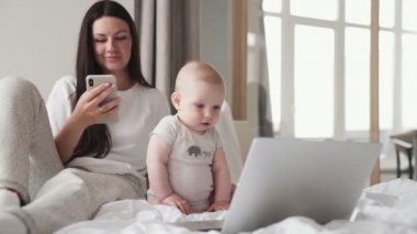 Küçük çocuk dizüstü bilgisayarda çizgi film izlerken annesi telefona bakıyor.