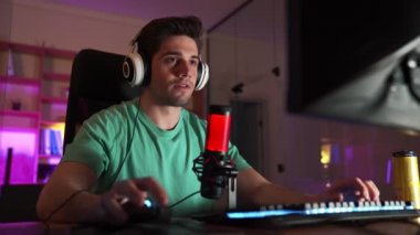 Profesyonel gülümseyen adam-oyuncu bilgisayarda oyun oynuyor ve zaferle seviniyor.