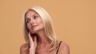 Bej stüdyoda kameraya poz veren olgun, güzel bir kadın.