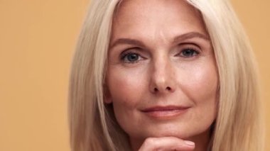 Düşünceli orta yaşlı bir kadının yandan bakıp bej rengi stüdyoda mükemmel tenini gösterişi.