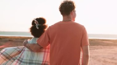 Çok uluslu bir çiftin sarılıp nehir kenarına gidişinin arka görüntüsü.