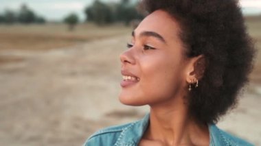 Nehir kıyısında dikilip etrafa bakan mutlu Afrikalı kadının yakından görüntüsü.