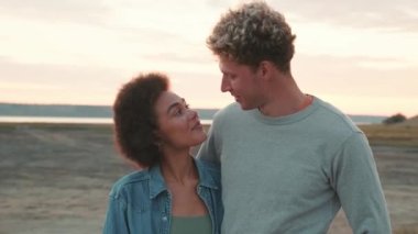 Gülümseyen çok uluslu çift haliçlerin arasında dururken birbirlerine ve kameraya bakıyor.