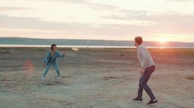 Gülümseyen çok uluslu çift haliçlerin arasında dururken birbirlerine frizbi atıyorlar.