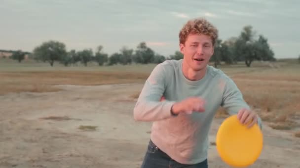 Lachender Gutaussehender Mann Wirft Frisbee Während Zwischen Der Mündung Steht — Stockvideo